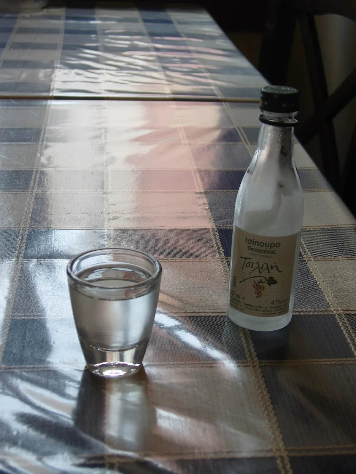 A bottle of tsipouro and a poured glass, on the taverna cloth