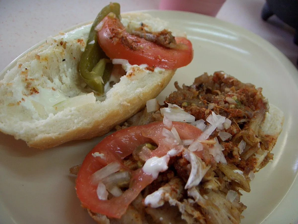 A lonche de pierna, opened up: roast pork leg, tomato, onion, and jalapeño on birote