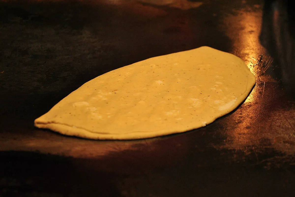 A quesadilla frying on the comal at a market stall