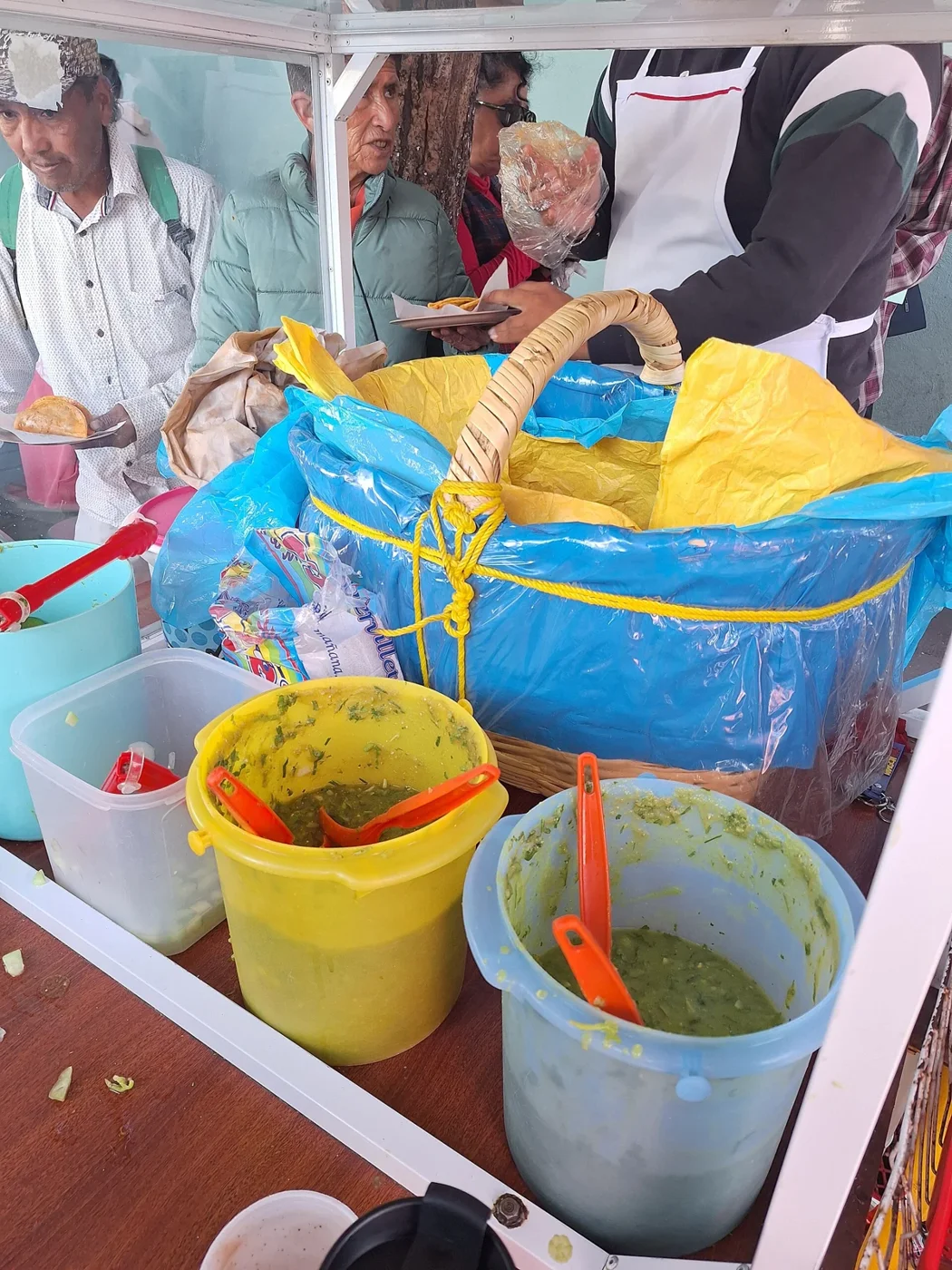 A tacos de canasta stall: the basket, the salsas, the line