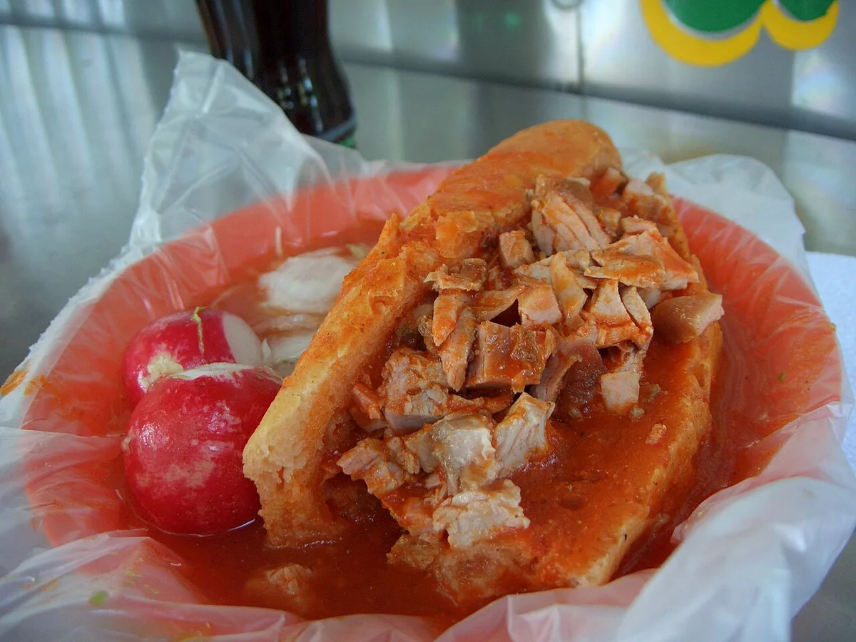 A torta ahogada: carnitas in a birote roll, drowned in tomato sauce, radishes on the side