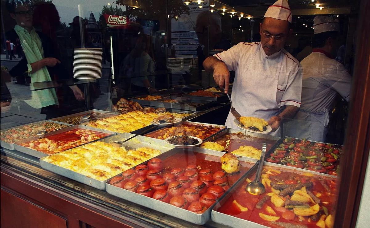 An esnaf lokantası chef serving the day's dishes from the bain marie